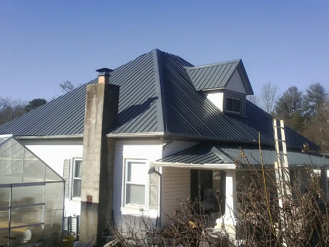 Dark blue standing seam metal roof on a white farmhouse with dormer — Slate & Tile Roof Repair by Roofing Brothers in Rio Rancho