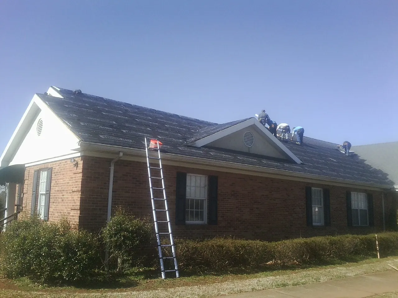 Crew tearing shingles off a brick ranch roof with a ladder set — Emergency Roof Repair work by our crew in Rio Rancho