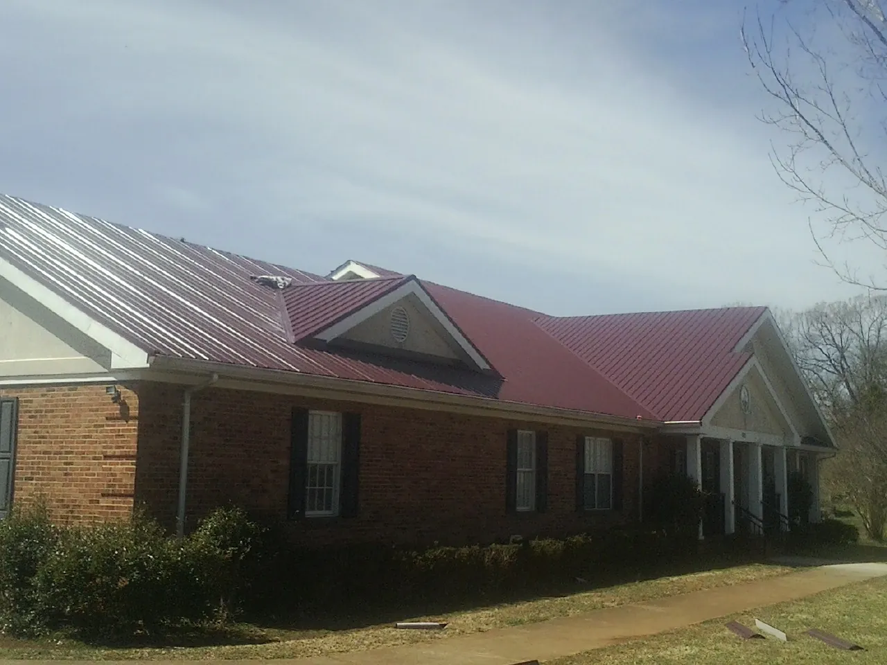 Red metal roof with gabled entries on a long brick building, from a Hail Damage Roof Repair job in Rio Rancho