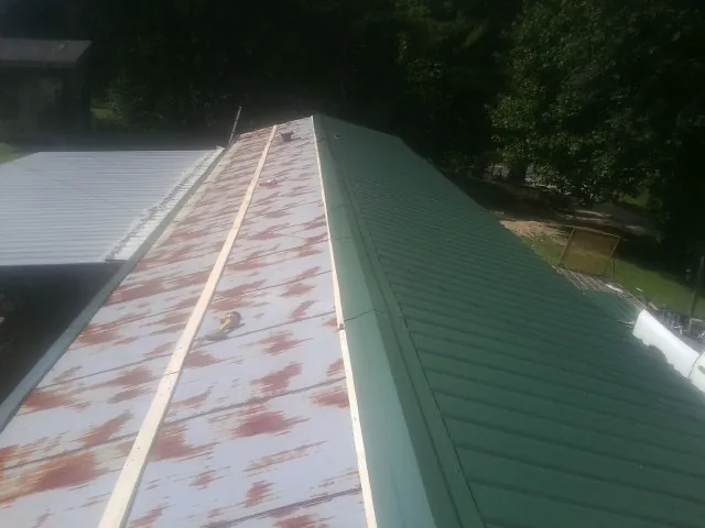 Old rusted panels beside newly installed green metal roofing — Wind Damage Roof Repair by Roofing Brothers in Rio Rancho