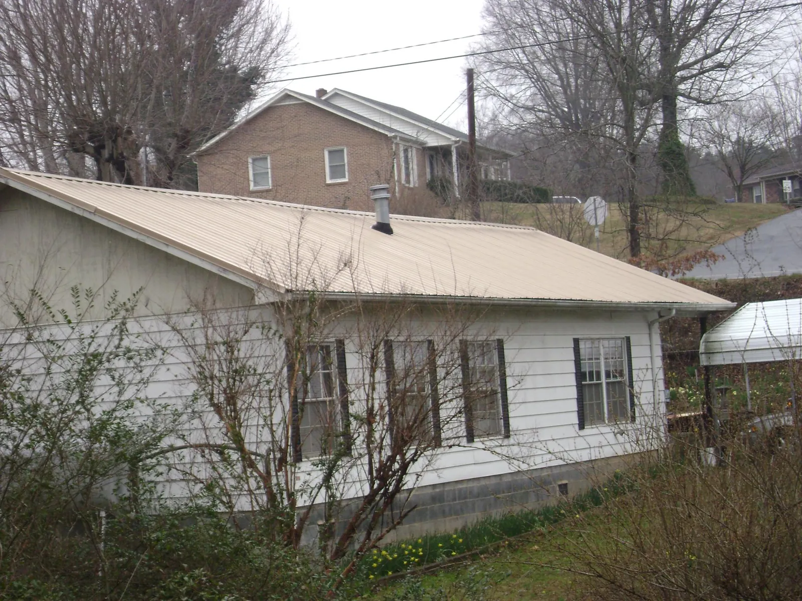 Tan metal roof on a white sided house set into a hillside — Commercial Roofing by Roofing Brothers in Rio Rancho